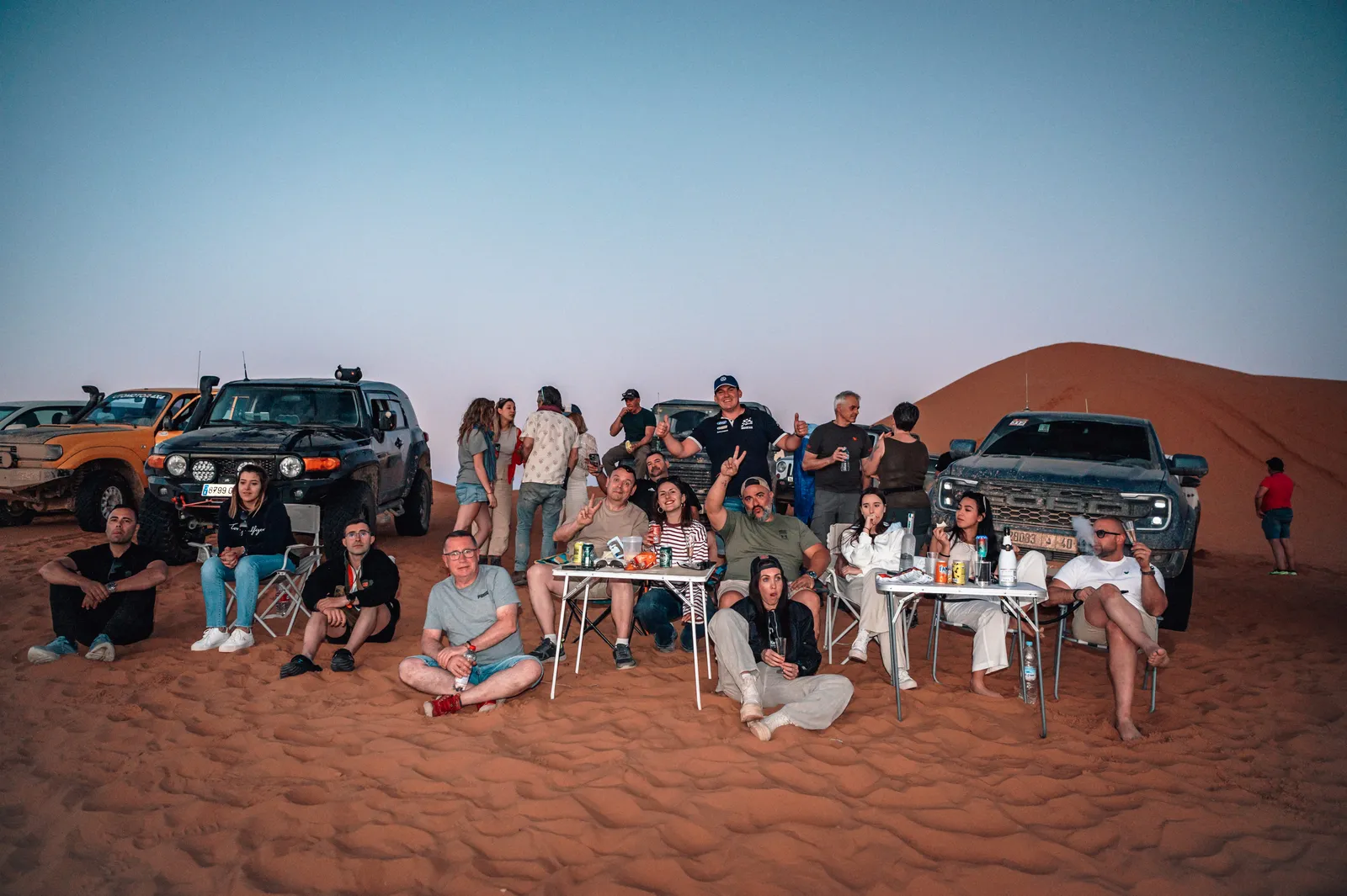 Grupo de viajeros reunidos en un campamento junto a las dunas al atardecer en Marruecos