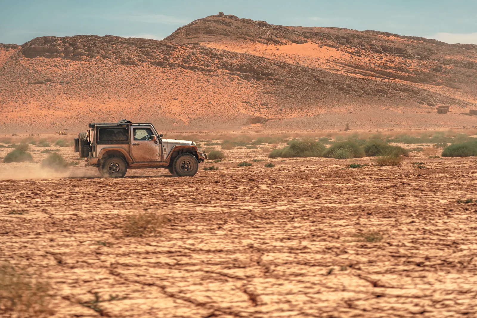 Jeep Wrangler solitario cruzando un valle de tierra agrietada junto a montañas del sur de Marruecos