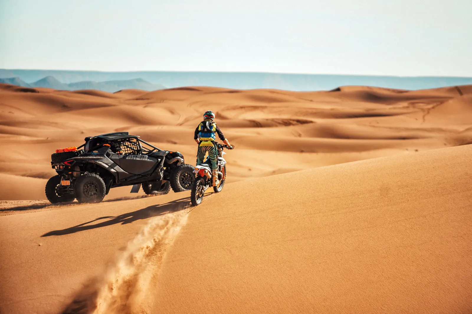 Motorista de enduro y buggy parados en una duna al atardecer en el desierto de Marruecos