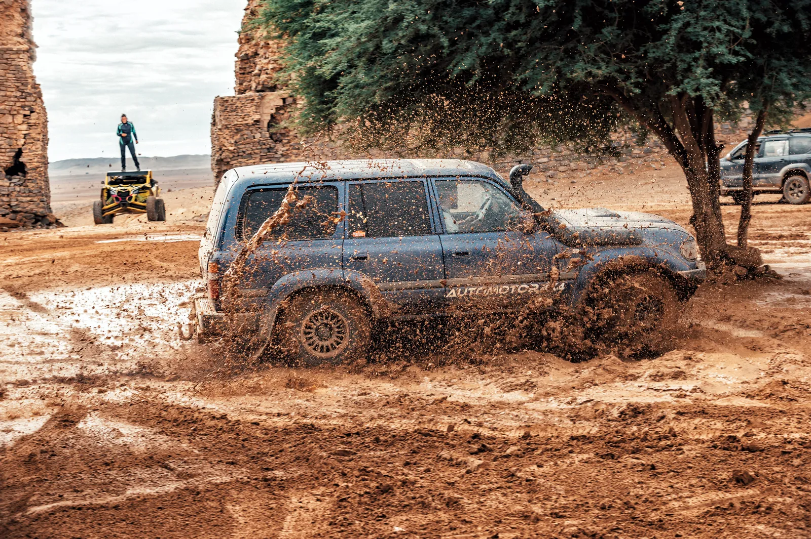 Toyota Land Cruiser cruzando un charco de barro junto a ruinas de adobe en Marruecos